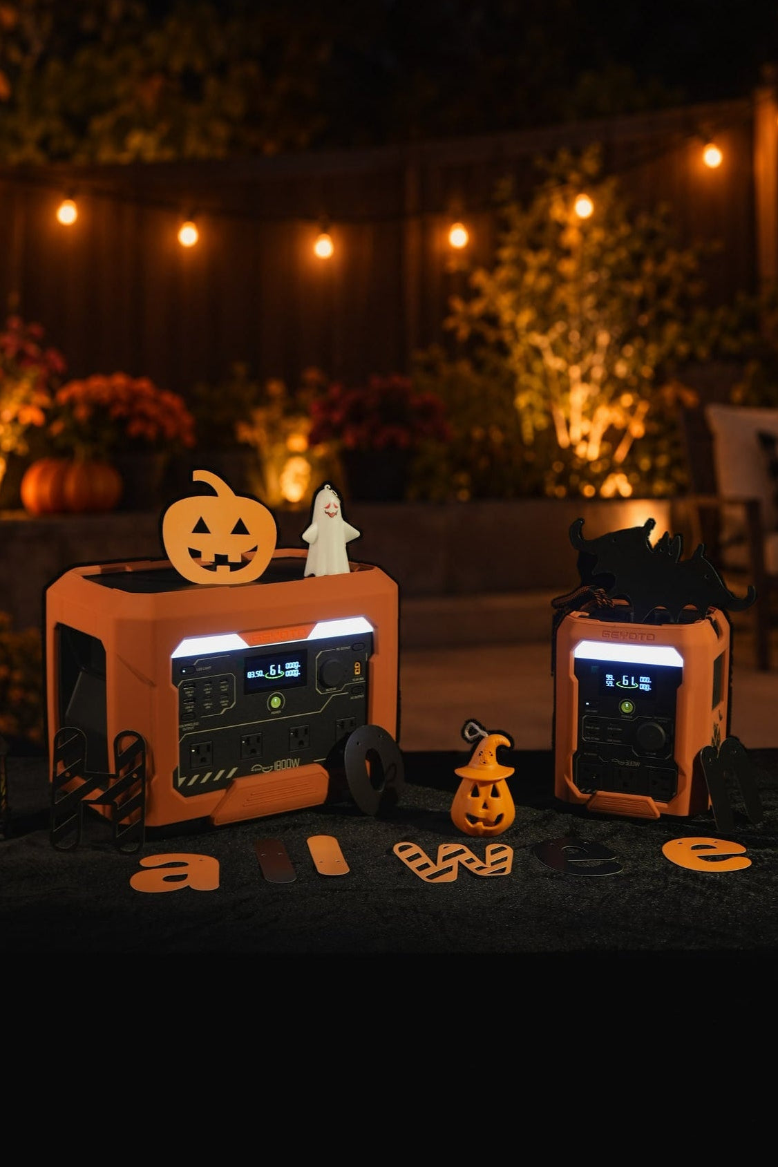 Two orange GEYOTO power stations surrounded by pumpkin and ghost decorations under warm string lights.