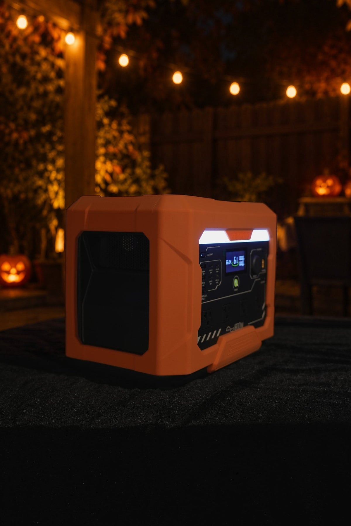 Side view of an orange GEYOTO power station under string lights in a Halloween-themed outdoor setting.