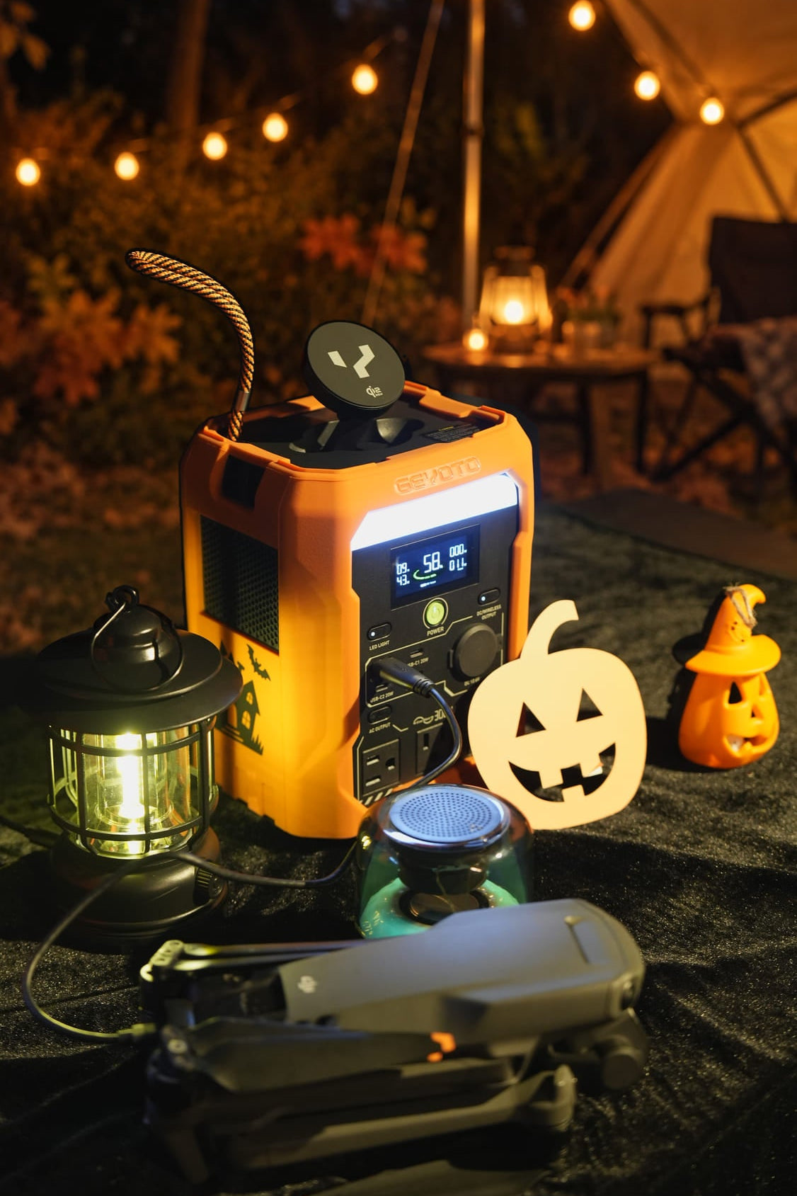 Orange GEYOTO power station beside a lantern, headphones, and a drone among Halloween decorations.