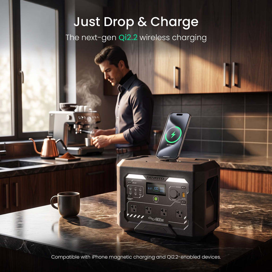 A portable power station sits on a kitchen counter with a smartphone placed on top, showing wireless charging compatibility. A man is visible in the background at a kitchen counter, and the scene is lit by warm natural light from a window.