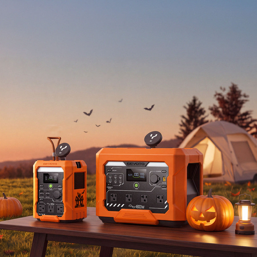 Two orange GEYOTO power stations beside jack-o'-lanterns and a lantern at a tent campsite at sunset.